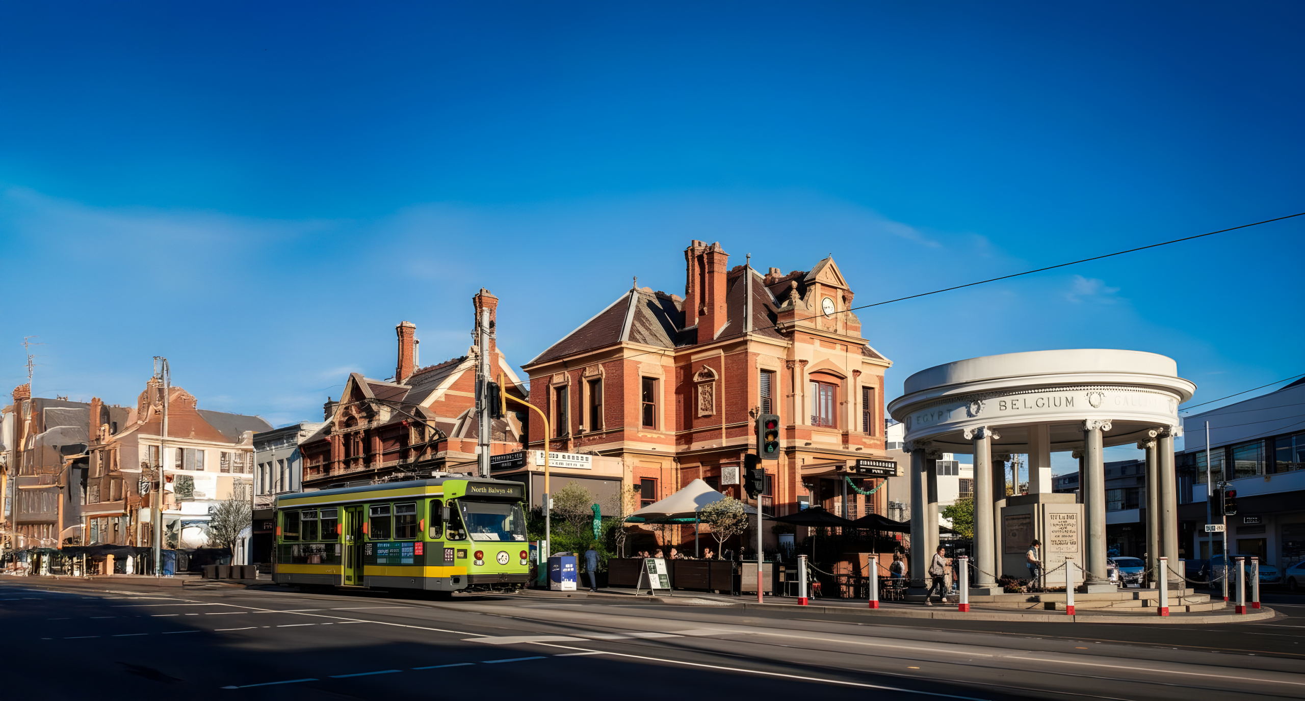 Historic buildings and a green tram on a sunny day in Melbourne. The scene includes a round monument and a painted building.