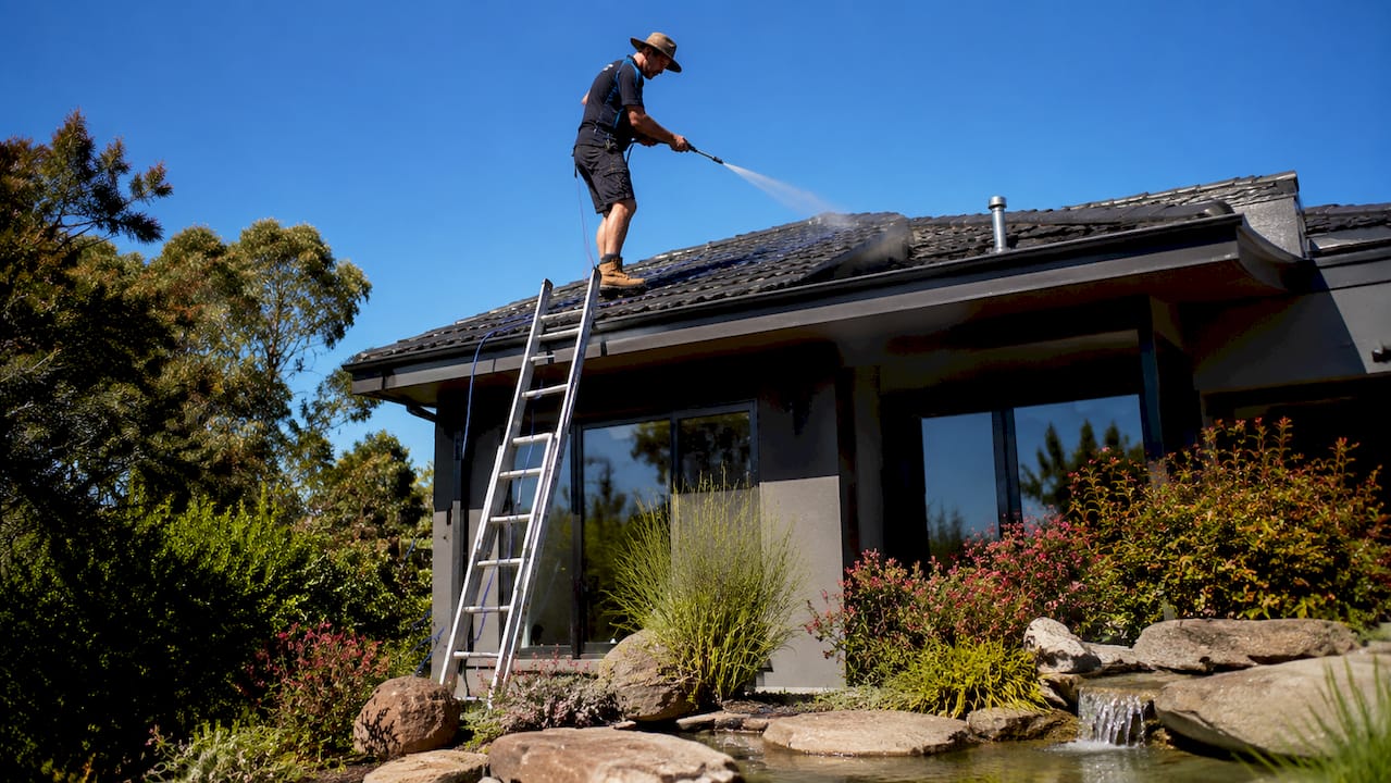 Man soft washing Melbourne roof on ladder