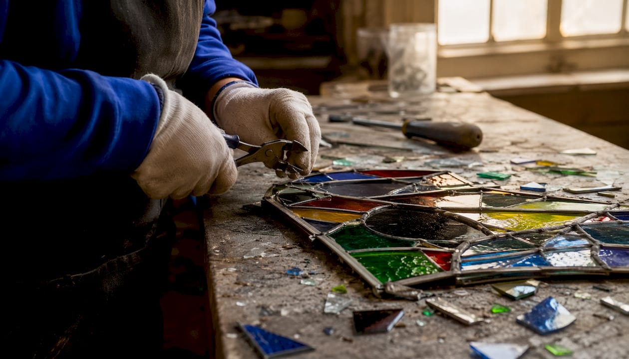 Hands dismantling stained glass panel on workbench