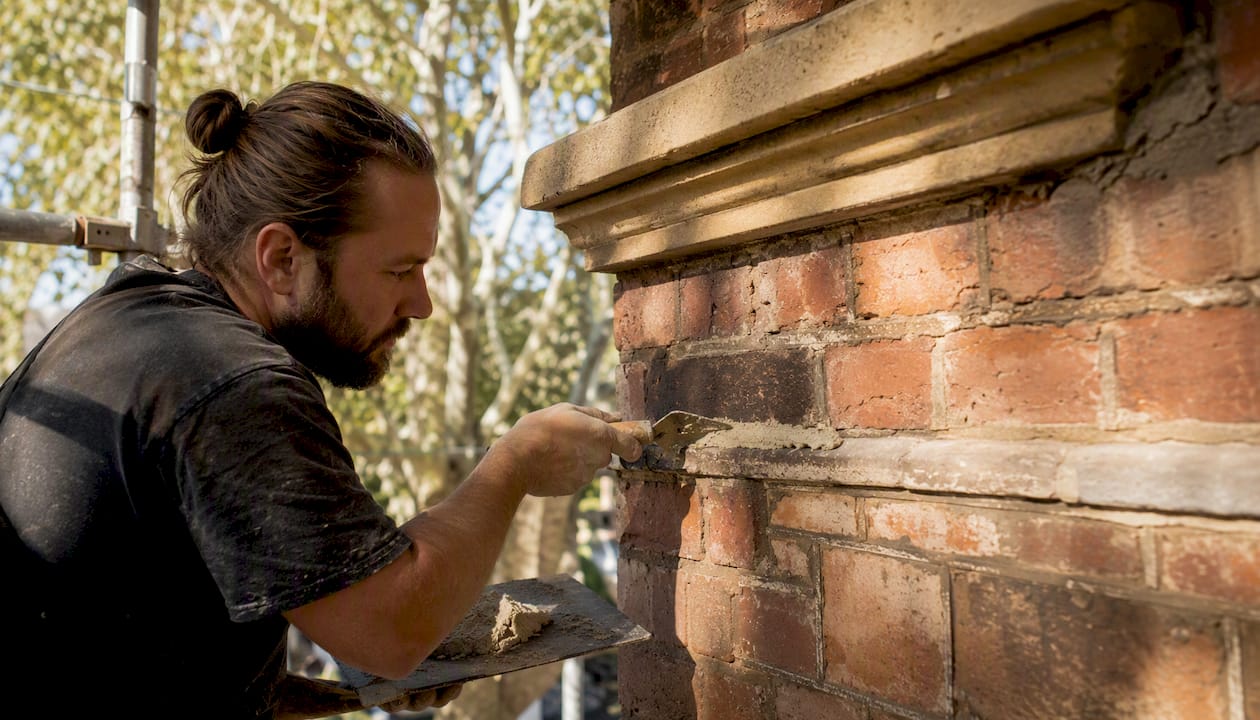 Hands applying lime mortar to heritage brickwork