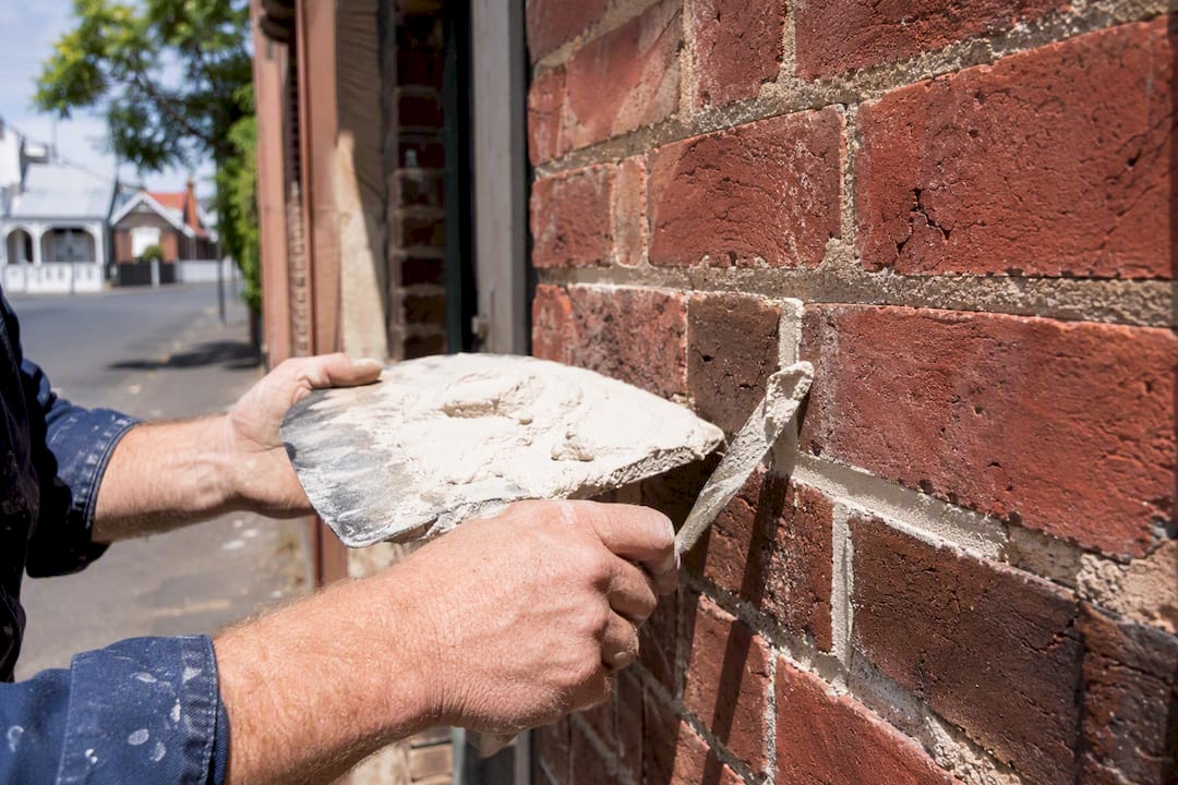 Hands repointing heritage brick wall with lime mortar