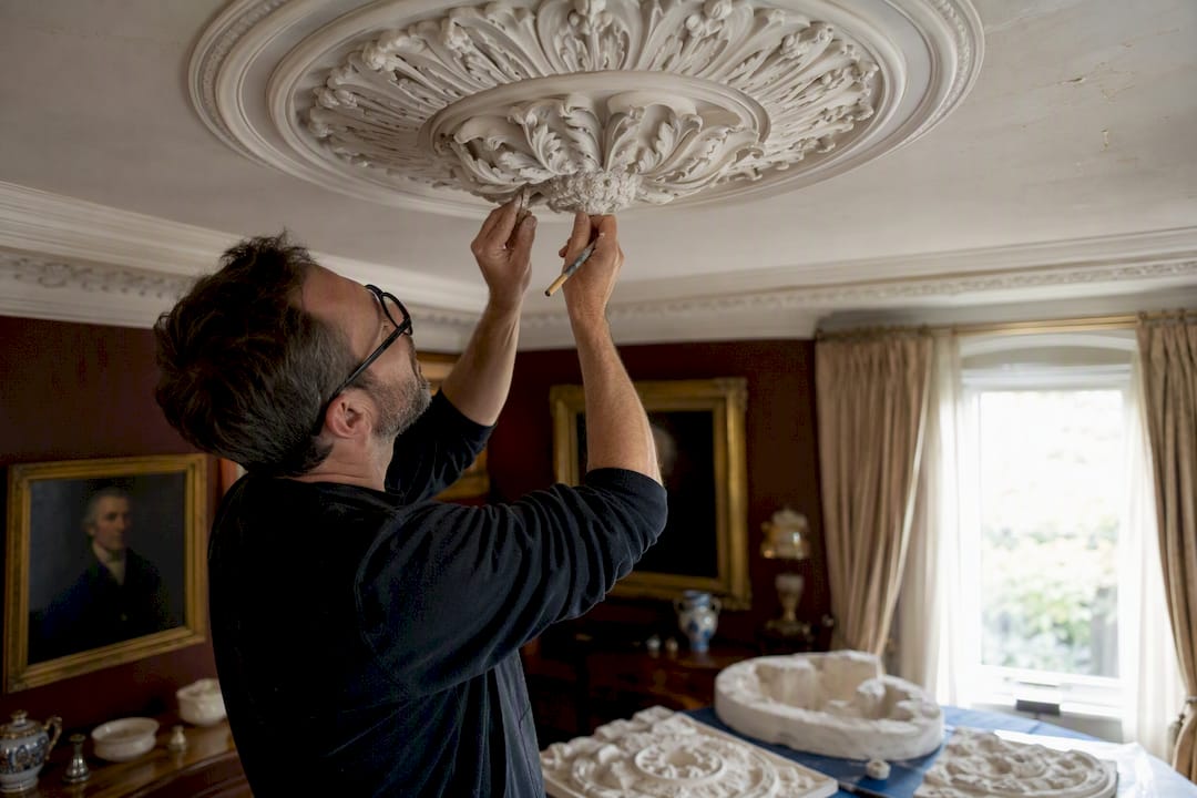 Hands restoring decorative plaster cornice moulding