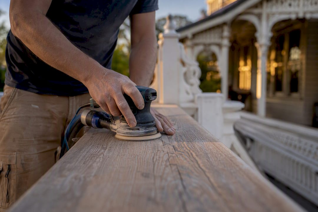 Hands sanding weathered timber deck boards
