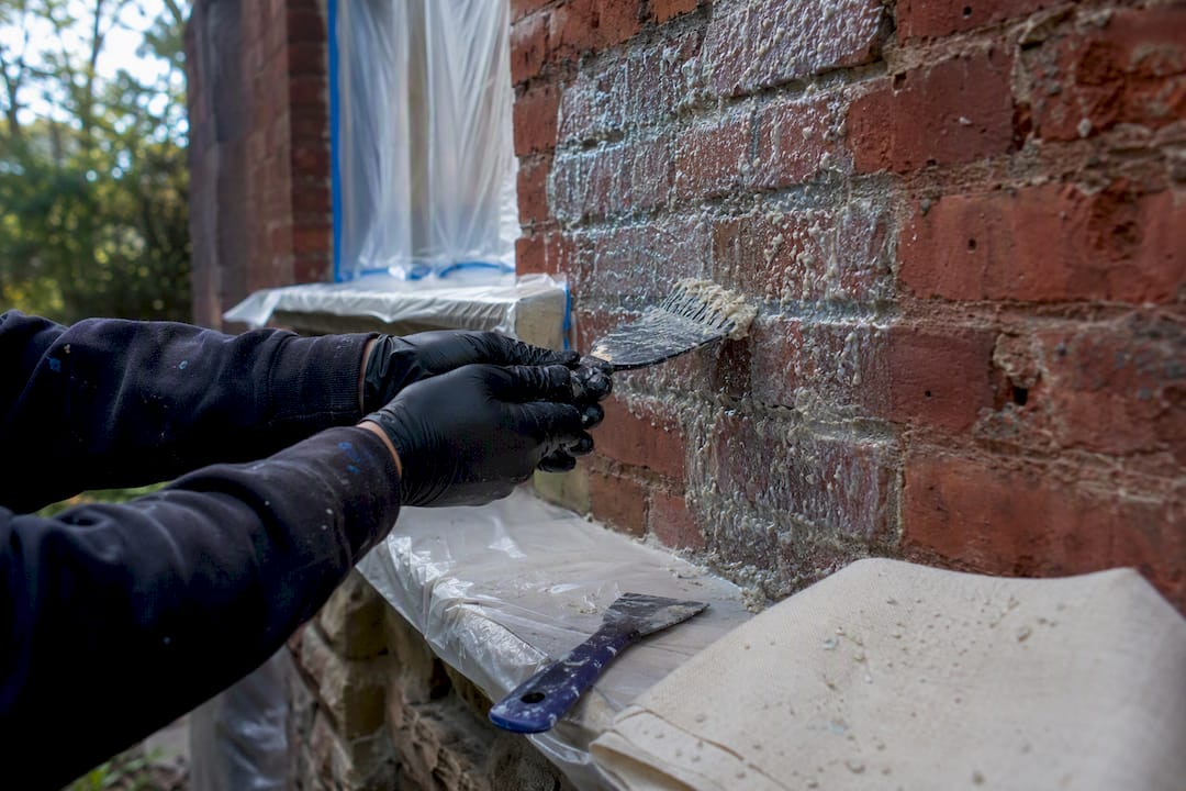 Hands applying paint stripper to brick wall